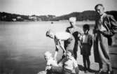 Från vänster: sittandes Alf och Leif Garthman, Rolf Karlsson (håller om Alf), Örjan och Bosse Stolt samt okänd står på bryggan vid Apels i Stensjön. Bilden är tagen under 1950-talet från Strandgatan. I bakgrunden ser man Gunnebobro och Lilla Berg.