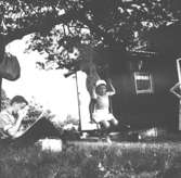 Familjen Garthman hälsar på hos Sven Torgé som har sommarstuga på Orust. Året är 1958. Leif-Åke Garthman sitter vid ett träd och dricker, brodern Alf Garthman står och Olle Torgé sitter på gungan.