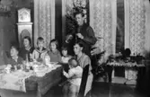 Julafton hemma hos familjen Viktor och Alma Karlsson på Kvarnfallet 31 med släkt. Tidigt 1930-tal. Från vänster: Alf och Rut Zakrisson, syskonen Ivar, Astrid och Margit, modern Alma med Rolf i famnen. Fadern Viktor (morfar till givaren) står upp.
