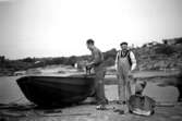 Pappa Helmer Garthman målar båten. I bakgrunden syns sönerna Alf och Leif som leker vid vattnet. Mannen i mitten är okänd av givaren. Näset, 1950-tal.