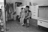 Tre barn som sitter på en liten pall framför en diskbänk. De tittar mot fotografen. Katrinebergs daghem, 1992-93.