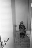 Dörren är öppen till en toalett på Katrinebergs daghem. Fotografen tar bilden utifrån på en liten flicka som sitter på toaletten med neddragna byxor. Till höger står ett handfat.