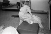 Ett litet barn, iklädd mjukiskläder, bäddar på golvet med kudde och sittkudde. Katrinebergs daghem, 1992.