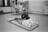Henrik rättar till filten efter att ha bäddat klart den mjuka madrassen med kudde. Madrassen ligger på golvet i ett lekrum. Lunkentussen, Katrinebergs daghem 1992.