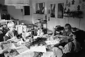 Fem barn sitter inomhus runt ett bord. De målar med vattenfärger på blad som ligger framför dem. Katrinebergs daghem, 1992.