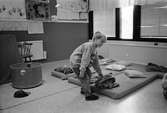 En pojke lutar sig ned och håller på en filt som ligger på en madrass på golvet. På madrassen ligger en kudde. Kanske dags för en liten sovstund? Katrinebergs daghem, 1992.