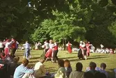 Ett folkdanslag som dansar på en gräsmatta vid Gunnebo slott. Runt omkring sitter människor och ser på.