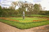 En gräsmatta med blommor längs kanterna och en skulptur i mitten. Gunnebo slottspark.
