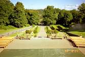 Träbänkar framför scenen vid Gunnebo slott. Parken i bakgrunden.