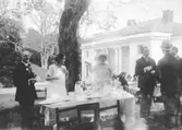 Internationellt pressbesök på Gunnebo slott den 22 juli 1923. Pressfolk ståendes utomhus vid ett kaffebord på Kejsareterrassen vid Gunnebo slott. Andra person från vänster är Margareta Sparre. Påskrift: 