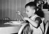 En pojke som äter mat på Holtermanska daghemmet 1953.