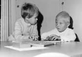 Två barn sitter vid ett bord där bland annat en kulram ligger. Holtermanska daghemmet 1953.