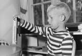 En pojke sitter vid ett bord hållandes en kulram i ena handen. Holtermanska daghemmet 1953.