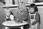 Tre flickor som sitter vid ett bord där det står en leksakstelefon. Holtermanska daghemmet 1953.