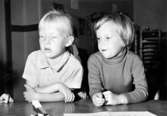 Två flickor som sitter vid ett bord. Bilden är något överexponerad. Holtermanska daghemmet 1953.