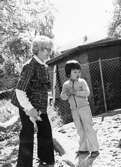 En lärarinna och ett dagbarn som står ute på lekplatsen vid Holtermanska daghemmet juni 1973.