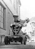 En pojke leker med trampbil på gårdsplanen utanför huset. I bakgrunden går en flicka. Holtermanska daghemmet juni 1973.