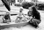 Tre barn och en fröken leker i sandlådan. Holtermanska daghemmet 1973.