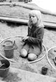 En flicka som leker med spänner och en rockring i sandlådan. Holtermanska daghemmet 1973.