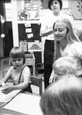Tre barn som ritar tillsammans med två fröknar. Holtermanska daghemmet maj 1975.