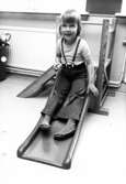 Ett barn som åker i en liten rutschkana inomhus. Holtermanska daghemmet maj 1975.
