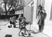Barn som leker utomhus och en fröken som tittar på. Holtermanska daghemmet, okänt årtal.