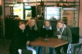 Fyra ungdomar sitter vid ett bord i ett café. Mölndalsbro i dag - ett skolpedagogiskt dokumentationsprojekt på Mölndals museum under oktober 1996. 1996_1283-1300 är gjorda av högstadieelever från Åbyskolan 8A, grupp 3. Se även 1996_0913-0940, gruppbilder på klasserna 1996_1382-1405 och bilder från den färdiga utställningen 1996_1358-1381.