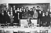 Grupporträtt framför svarta tavla i en skolsal, cirka 1937-1940. Troligtvis återträff av klasskamrater. Okänd plats.