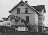 Grävmaskin i färd med att riva Karlssons järnhandel (E & K. Karlssons järnhandel) på Kungsbackavägen 6 år 1974.