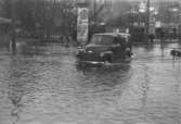 Översvämning 1951 (sett västerifrån) i korsningen mellan Kvarnbygatan-Frölundagatan och Göteborgsvägen-Kungsbackavägen. En bil kör ut i korsningen från Kvarnbygatan. Till vänster ses Pressbyråns kiosk.