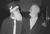 En jultomte kramar om en manlig boende. Mannen ler. Okänt årtal.