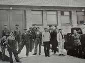 Tretton män står uppställda framför en byggnad. Okänt plats och årtal.