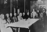 Män och kvinnor samt ett barn som sitter och står omkring ett bord. Okänt årtal.