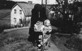 Mormor Nora Krantz hjälper Karin Pettersson (gift Hansson) att cykla på sin nya trehjuling, Torrekulla 1948.