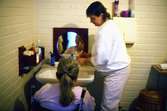 En person ser sig i spegeln efter att nyligen ha blivit klippt på Stretereds vårdhem för handikappade, 1980-talet.