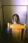 En kvinna med fläta sitter på en trästol framför en tegelvägg, troligen på Sagåsen 1980-tal.