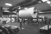Män i arbete med pappersbal.
Bilden är tagen vid Kartongmaskin 2. Bilden ingår i serie från produktion och interiör på pappersindustrin Papyrus, 1980-talet.