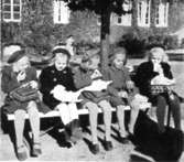 Fem flickor sitter på en bänk och har matrast utanför Kvarnbyskolan (Centralskolan), okänt årtal. Avfotograferad ur 