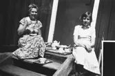 Till vänster sitter Eivor Bjerrhede  (1921 - 2015) och till höger sitter hennes systerdotter Monica Cedstrand (f. 1940) vid Vommedal Östergård 