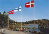 Ett vykort med utsikt över Stensjön, omkring 1967. Ett sällskap sitter och fikar vid fyra flaggstänger med flaggor från Sverige, Norge, Finland och Danmark. Bak på kortet står anteckningen: 