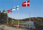 Ett vykort med utsikt över Stensjön, omkring 1967. Ett sällskap sitter och fikar vid fyra flaggstänger med flaggor från Sverige, Norge, Finland och Danmark. Bak på kortet står anteckningen: 