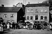 Människor och hästomnibussen står på Mölndals torg (senare: Gamla torget), okänt årtal. I bakgrunden ses från vänster Kvarnbygatan 39 och 41 som var Viktualieföreningens affär (senare: brandstation och garage för polisbilar och Mölndals målarskola). Kvinnorna som står till höger har med sig mjölkkannor.