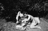 En man och en kvinna sitter på en filt och fikar, troligtvis vid Tulebosjön cirka 1930.