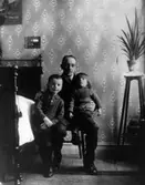 Helmer med Ivar och Inge i hemmet Klockaregården B2B2, troligen taget 1917. Obs! den praktfulla sängen (hemmets klenod?) vidare liljeväxten som sköttes så att den aldrig(!) vissnade och den huvudstora kaktusen nederst på piedestalen.

