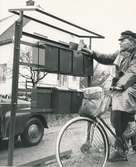 Fotografi av norsk brevbärare som delar ut post från sin cykel.