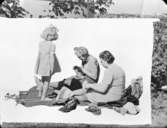 Två kvinnor och en flicka sittande på en filt