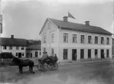 Häst och vagn framför lägenhetshus med affärer vid Vetlanda torg.