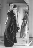 Modell i aftonklänning i sammet och flerradigt pärlhalsband. Modell i mönstrad klänning i spegelbilden. Av Maggy Rouff.