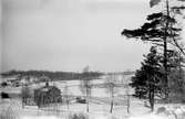 Utsikt över snöiga åkrar och ett par bostadshus.