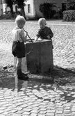 Västra Torget i Jönköping. Två pojkar leker vid vattenhon, som fanns för att stadens hästar skulle kunna vederkvicka sig. Husen i bakgrunden är Tändsticksbolagets arbetarbostäder, de så kallade Bostäderna.